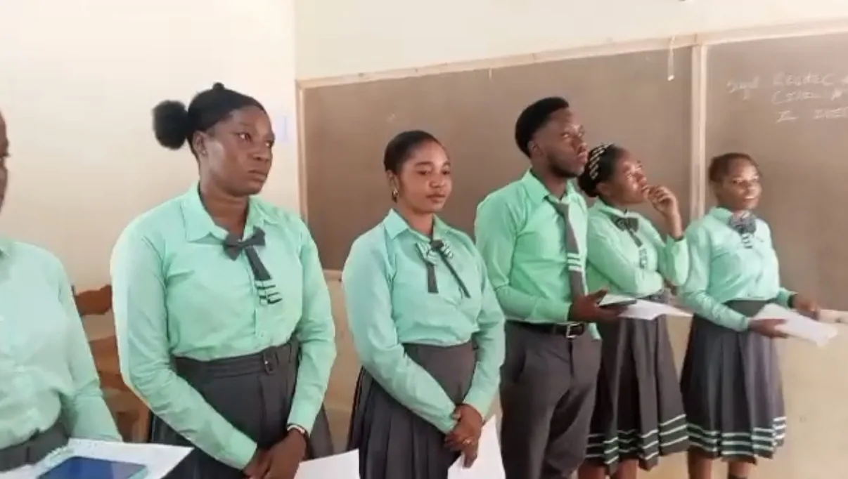 Older students in green uniforms stand together in their classroom