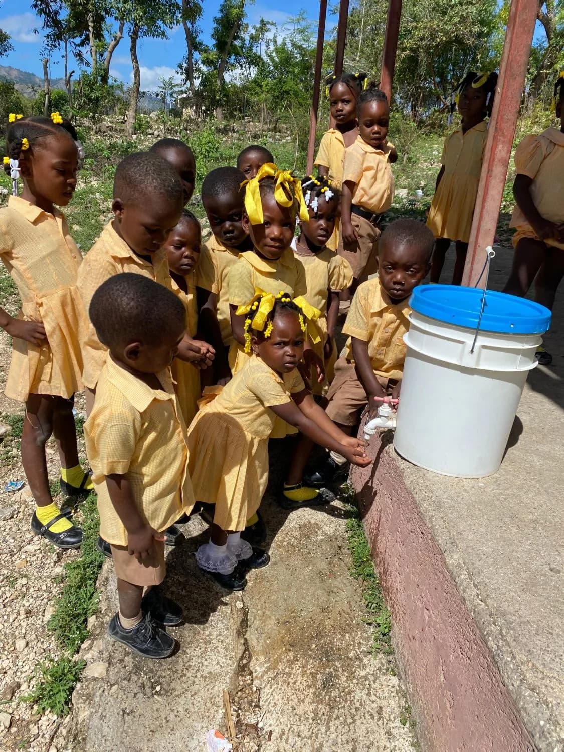 Young students in yellow uniforms take turns washing their hands at a school water station